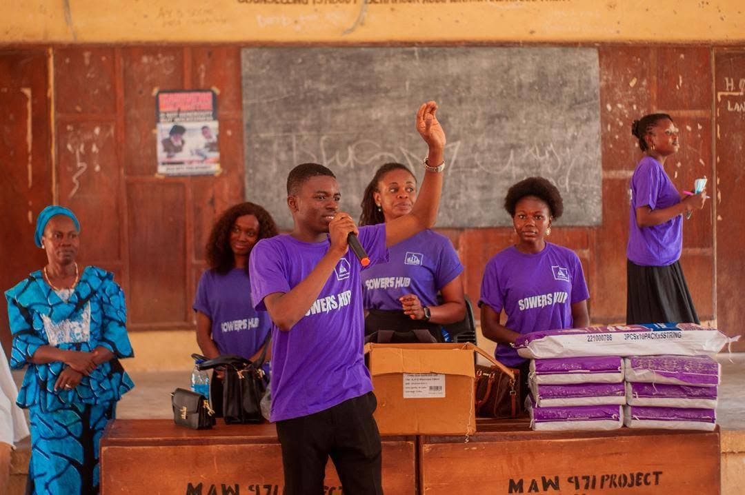 The SowersHub team speaking to a school hall with sanitary pads stacked ready to hand out